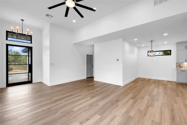 unfurnished living room featuring light hardwood / wood-style floors, ceiling fan with notable chandelier, and a towering ceiling