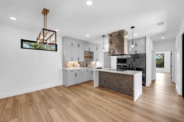 kitchen with stainless steel appliances, a kitchen island, light wood-type flooring, and pendant lighting