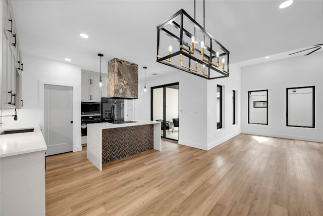 kitchen with black appliances, a barn door, decorative light fixtures, light wood-type flooring, and white cabinetry