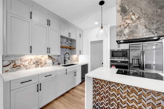 kitchen featuring tasteful backsplash, appliances with stainless steel finishes, sink, light wood-type flooring, and decorative light fixtures