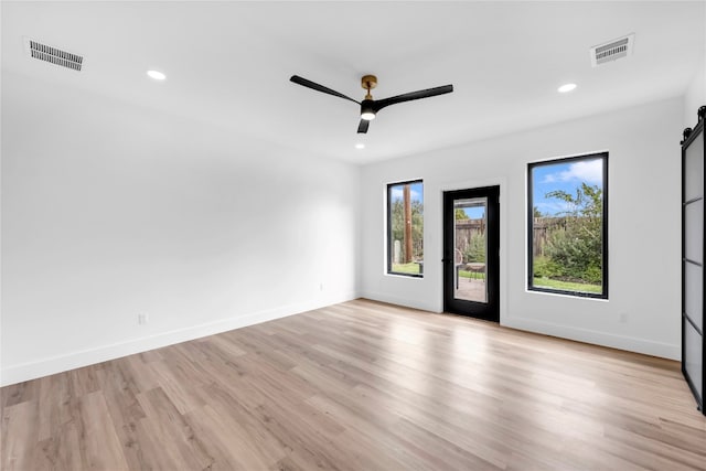 empty room with a barn door, light hardwood / wood-style floors, and ceiling fan