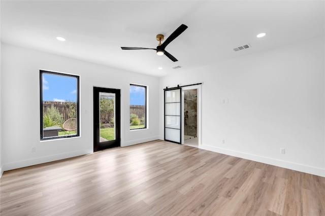 unfurnished room featuring a barn door, light hardwood / wood-style floors, and ceiling fan