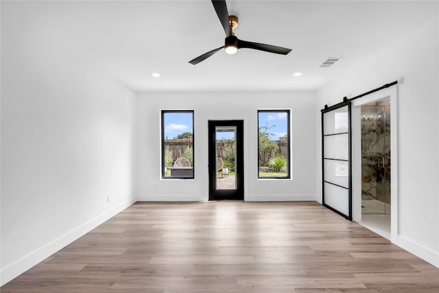 spare room featuring light hardwood / wood-style floors, a barn door, and ceiling fan