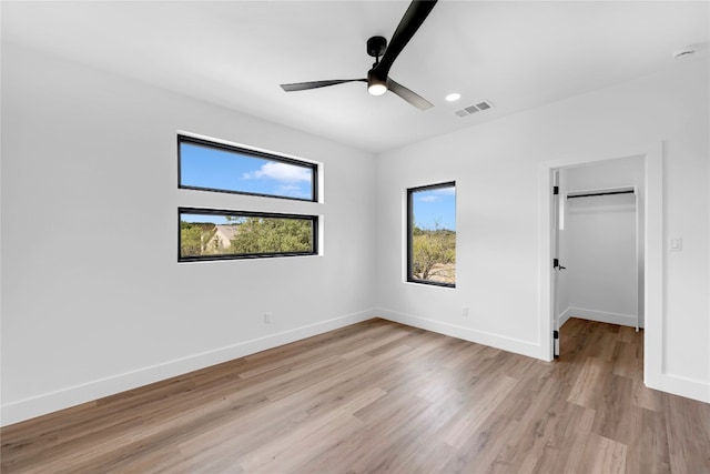 unfurnished bedroom with a closet, ceiling fan, a spacious closet, and light hardwood / wood-style floors