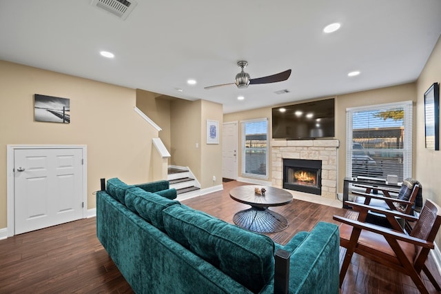 living room featuring a stone fireplace, dark wood-type flooring, and ceiling fan