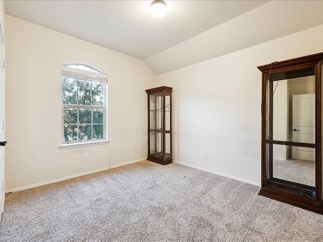 empty room with a textured ceiling, carpet flooring, and vaulted ceiling