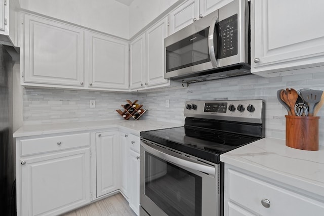 kitchen with stainless steel appliances, light stone countertops, white cabinets, and backsplash