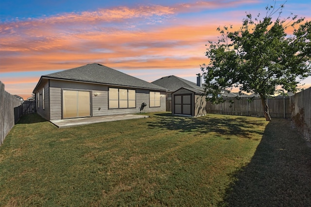 back house at dusk featuring a storage unit, a yard, and a patio area