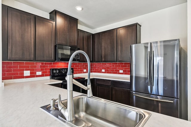 kitchen featuring dark brown cabinetry, backsplash, stainless steel refrigerator, and sink