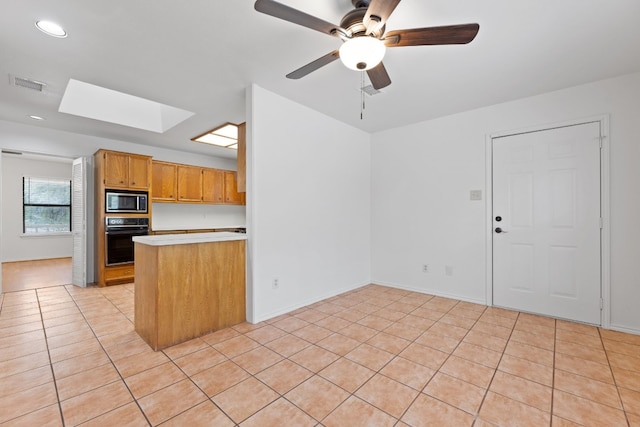 kitchen featuring stainless steel microwave, kitchen peninsula, black oven, a skylight, and ceiling fan