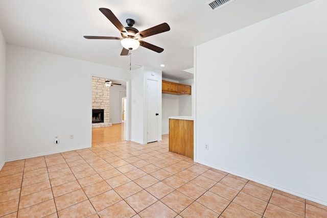 empty room featuring a stone fireplace, light tile patterned floors, and ceiling fan