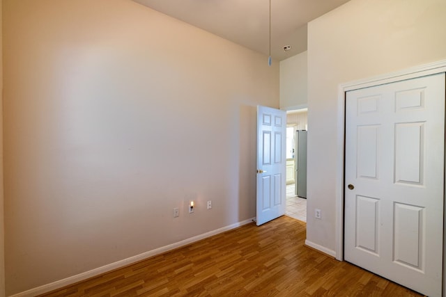 unfurnished bedroom featuring stainless steel fridge, a high ceiling, hardwood / wood-style flooring, and a closet