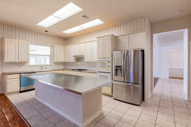 kitchen featuring decorative backsplash, light tile patterned floors, a kitchen island, sink, and stainless steel appliances