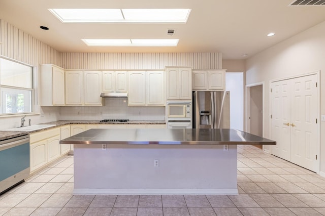 kitchen with stainless steel counters, sink, a kitchen island, stainless steel appliances, and light tile patterned floors