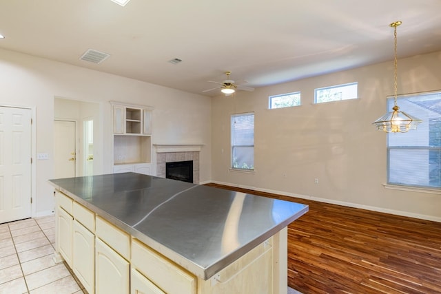 kitchen with cream cabinetry, light wood-type flooring, ceiling fan with notable chandelier, a tile fireplace, and pendant lighting