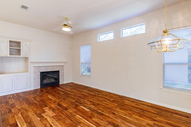 unfurnished living room featuring ceiling fan with notable chandelier, wood-type flooring, and a fireplace