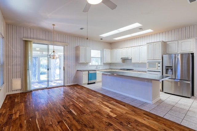 kitchen featuring white cabinets, decorative light fixtures, light wood-type flooring, appliances with stainless steel finishes, and ceiling fan with notable chandelier