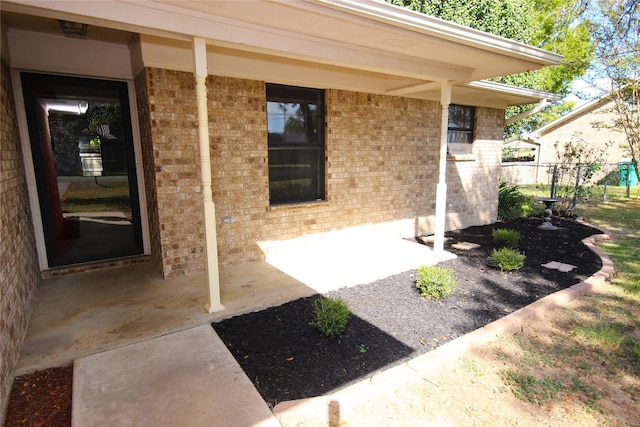 view of exterior entry with fence and brick siding