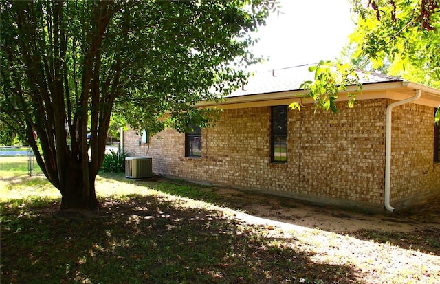 view of home's exterior featuring brick siding, central air condition unit, and fence