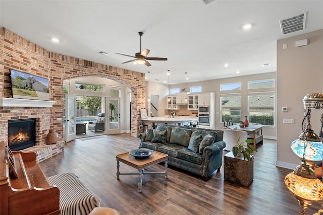 living room featuring dark wood-type flooring, a healthy amount of sunlight, and a brick fireplace