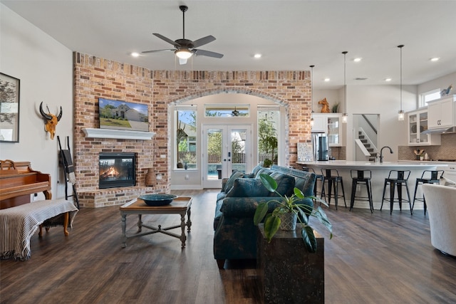 living room with french doors, ceiling fan, a brick fireplace, and dark hardwood / wood-style flooring