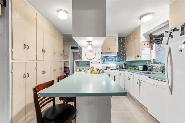 kitchen featuring cream cabinets, tasteful backsplash, a kitchen breakfast bar, sink, and white appliances