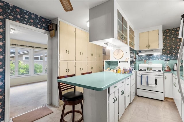 kitchen with light carpet, kitchen peninsula, white gas stove, a breakfast bar, and white cabinets