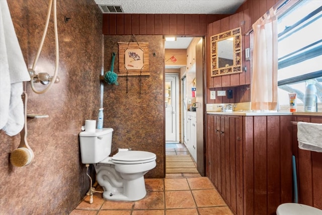 bathroom with vanity, wooden walls, a textured ceiling, and toilet