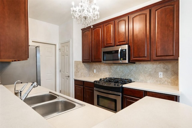 kitchen with appliances with stainless steel finishes, pendant lighting, sink, backsplash, and a notable chandelier