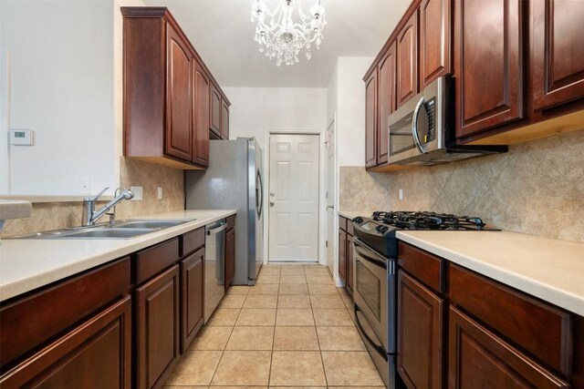 kitchen with sink, light tile patterned floors, appliances with stainless steel finishes, backsplash, and decorative light fixtures