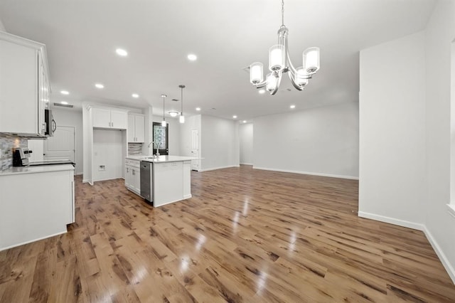 kitchen featuring tasteful backsplash, an island with sink, white cabinetry, pendant lighting, and stainless steel dishwasher