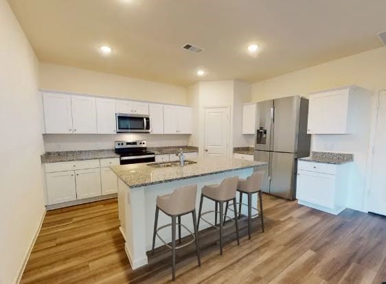 kitchen featuring a kitchen island with sink, white cabinets, stainless steel appliances, and light wood-type flooring