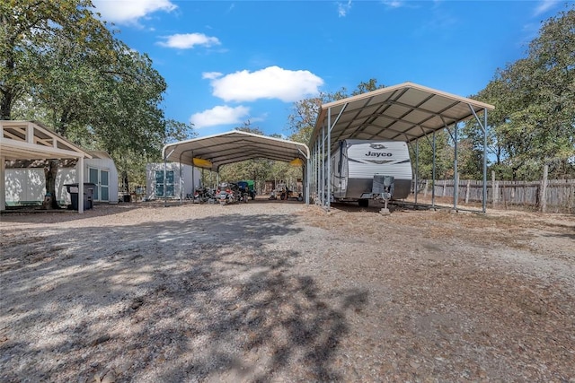 view of car parking with a storage shed, fence, a carport, and driveway