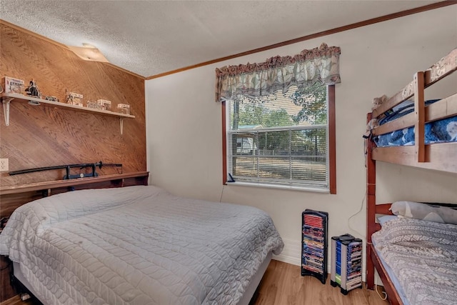 bedroom with ornamental molding, a textured ceiling, wood finished floors, and wooden walls