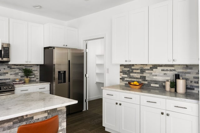 kitchen featuring appliances with stainless steel finishes, light stone countertops, backsplash, white cabinets, and dark wood-type flooring