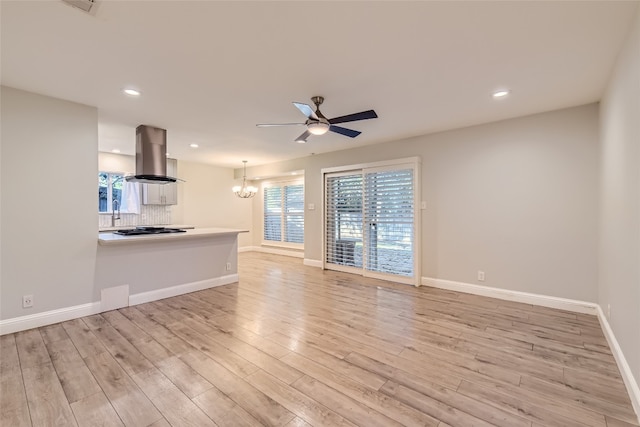 unfurnished living room with ceiling fan with notable chandelier and light wood-type flooring