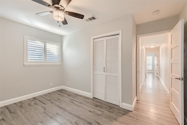 unfurnished bedroom with multiple windows, a closet, light wood-type flooring, and ceiling fan