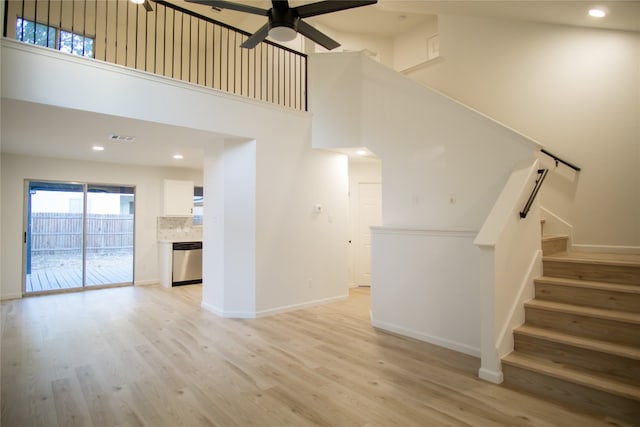 unfurnished living room with a high ceiling, light wood-type flooring, and ceiling fan