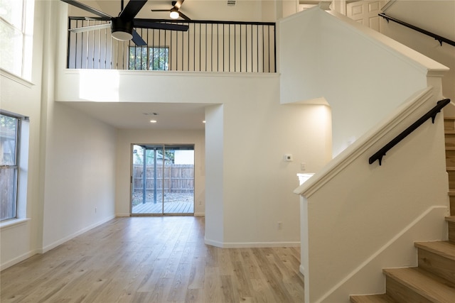 stairs with ceiling fan, a high ceiling, and hardwood / wood-style floors