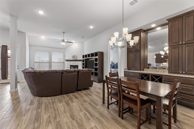 dining room with a stone fireplace, light hardwood / wood-style floors, and ceiling fan with notable chandelier