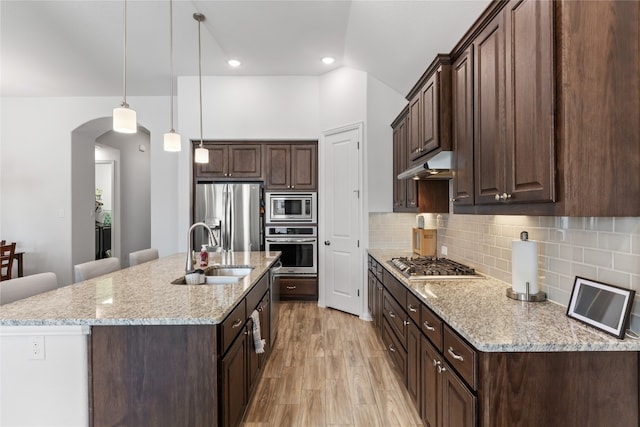 kitchen with sink, light stone countertops, an island with sink, decorative light fixtures, and stainless steel appliances