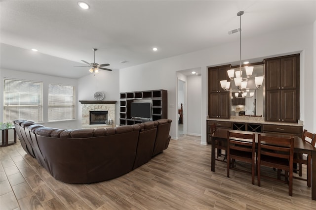 living room featuring ceiling fan with notable chandelier, light hardwood / wood-style floors, and a stone fireplace