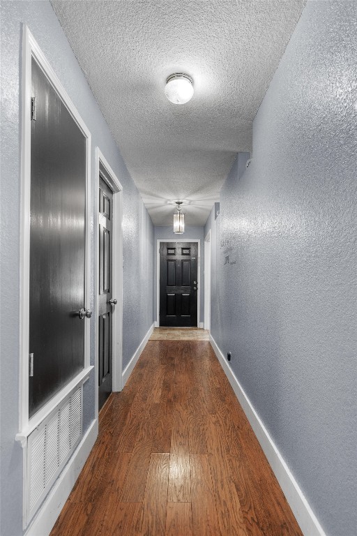 hall with a textured ceiling and dark hardwood / wood-style floors