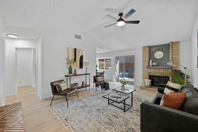 living room with lofted ceiling, ceiling fan, a textured ceiling, a brick fireplace, and light hardwood / wood-style floors