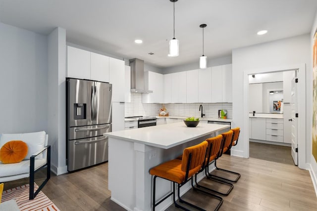 kitchen with white cabinetry, a kitchen island, wall chimney range hood, and appliances with stainless steel finishes