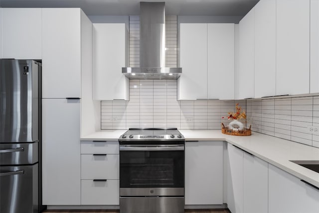 kitchen featuring decorative backsplash, white cabinets, stainless steel appliances, and wall chimney range hood