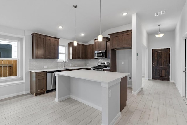 kitchen with a center island, sink, vaulted ceiling, appliances with stainless steel finishes, and decorative light fixtures