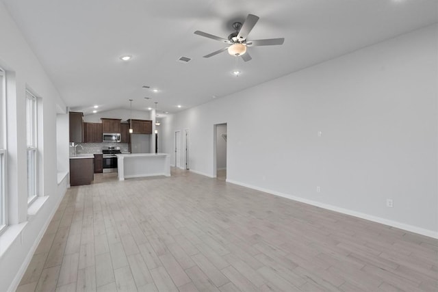 unfurnished living room with ceiling fan, light hardwood / wood-style floors, sink, and vaulted ceiling