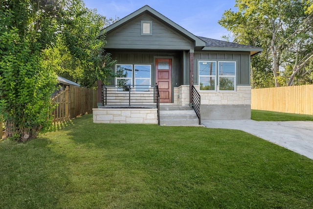 view of front of property featuring board and batten siding, a front yard, stone siding, and fence