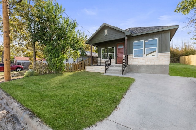 view of front of property with board and batten siding, a front yard, stone siding, and fence